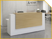 Modern white reception desk with a light wood front panel in a corporate lobby, with a sign reading 'Aether' in the background behind the desk.