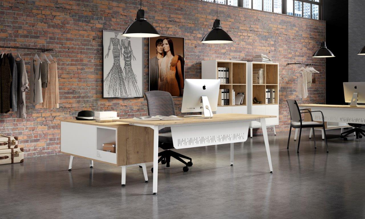 Open loft-style design studio with brick wall, two desks, iMacs, and clothing on racks adjacent to storage shelves.