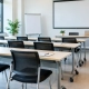 Mobiliario para salas de formación que funciona | OfficeDeco Empty training room with rows of light desks, black mesh chairs, a large projection screen, flip chart, and a laptop on the front table.